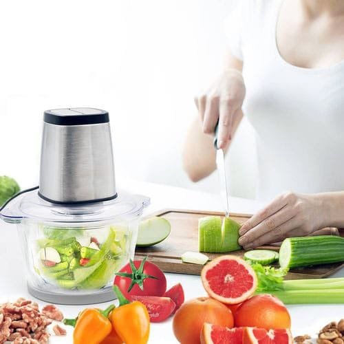 A pair of hands cutting vegetables next to a food processor