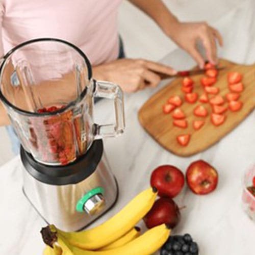 Woman making delicious smoothie with blender at white marble tabl