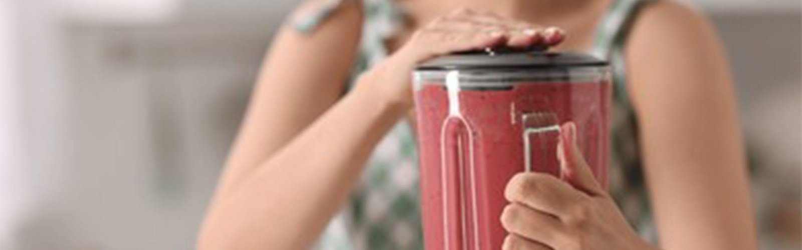 Woman making delicious smoothie with blender in kitchen, closeup