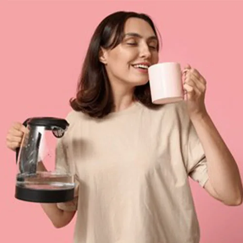 Beautiful young woman with modern electric kettle and cup on pink
