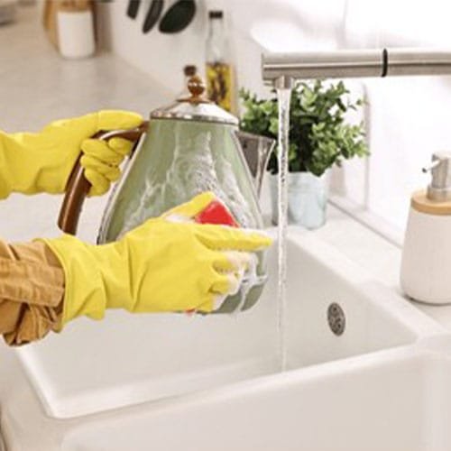 Woman washing electric kettle with sponge at sink in kitchen, clo